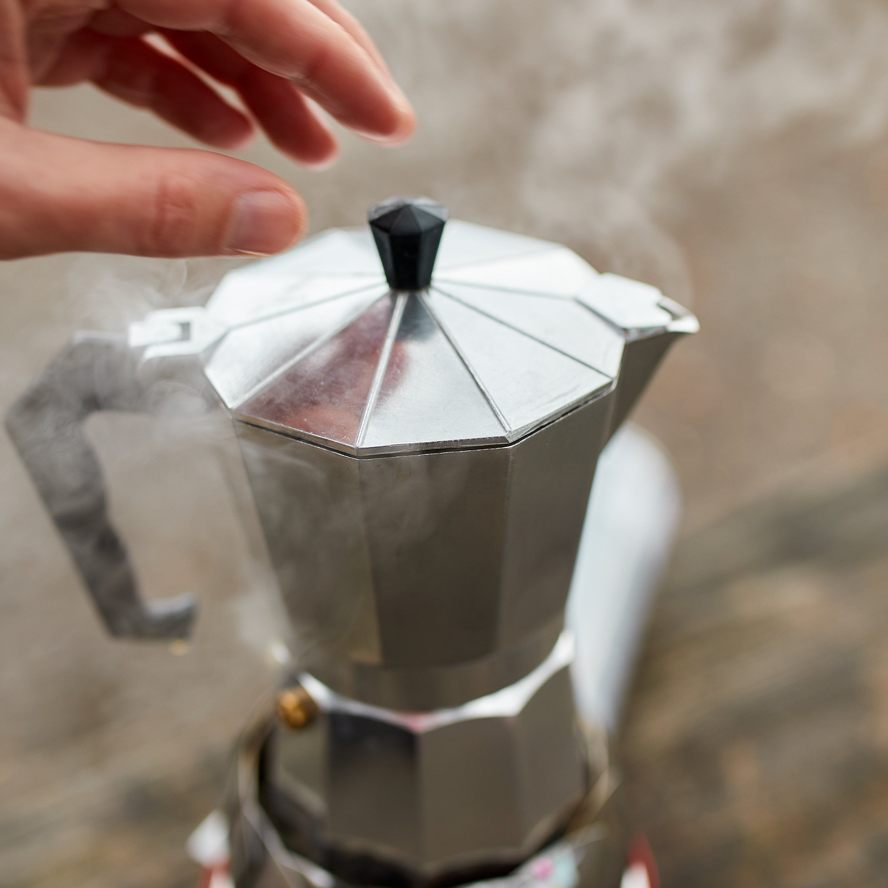 Brewing coffee in a coffee pot with one hand reaching to lift the top lid.