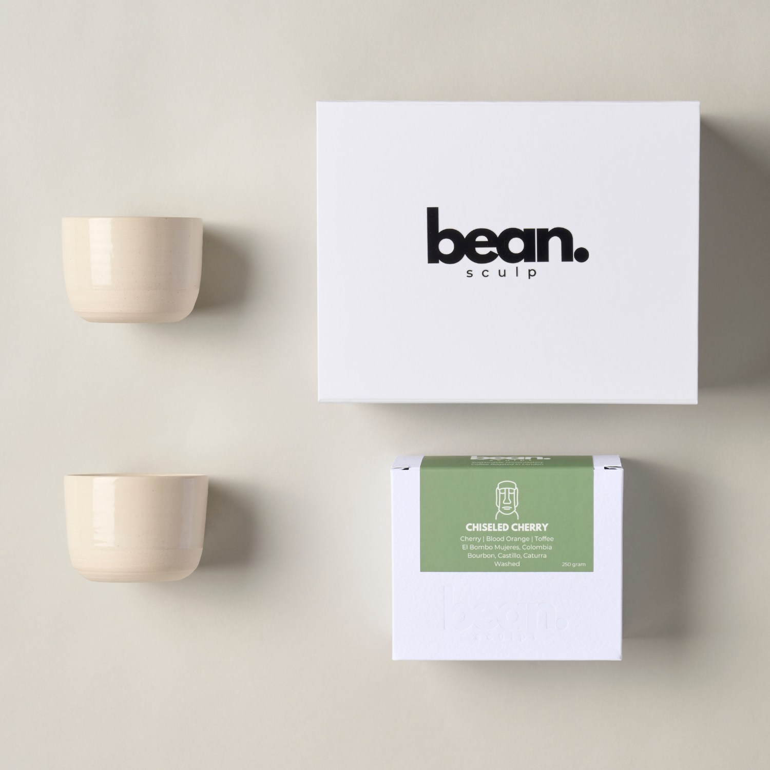 A bundle showing one white bean sculpt box, one Bean Sculpt speciality coffee and two handcrafted beige stoneware Flat White Tumblers with a minimalist design, ideal for espresso lat white drinks. 