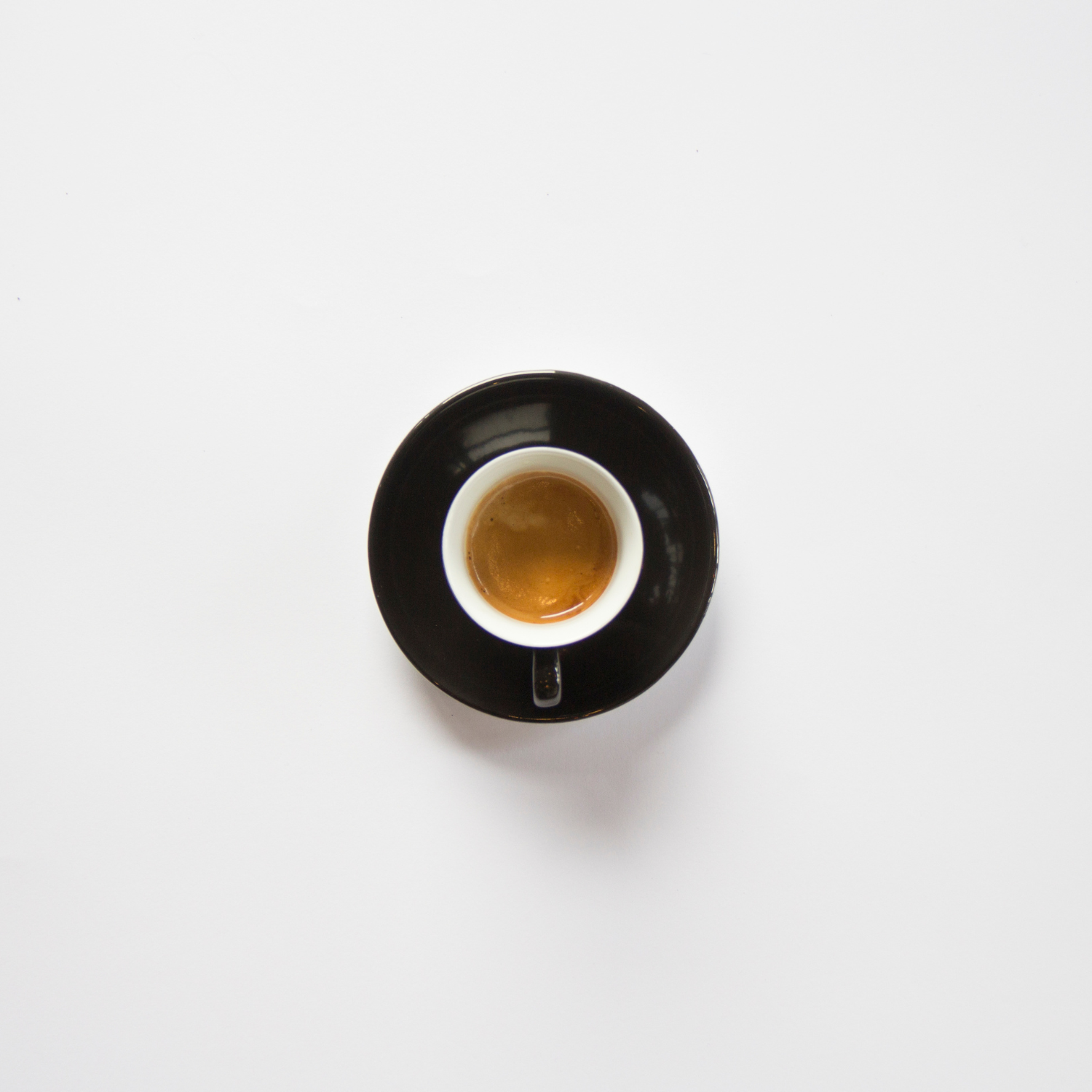 Top-down view of a perfect espresso in a white cup with a black saucer on a pure white table. Smooth and rich, made from a Colombian single-origin decaf coffee. 