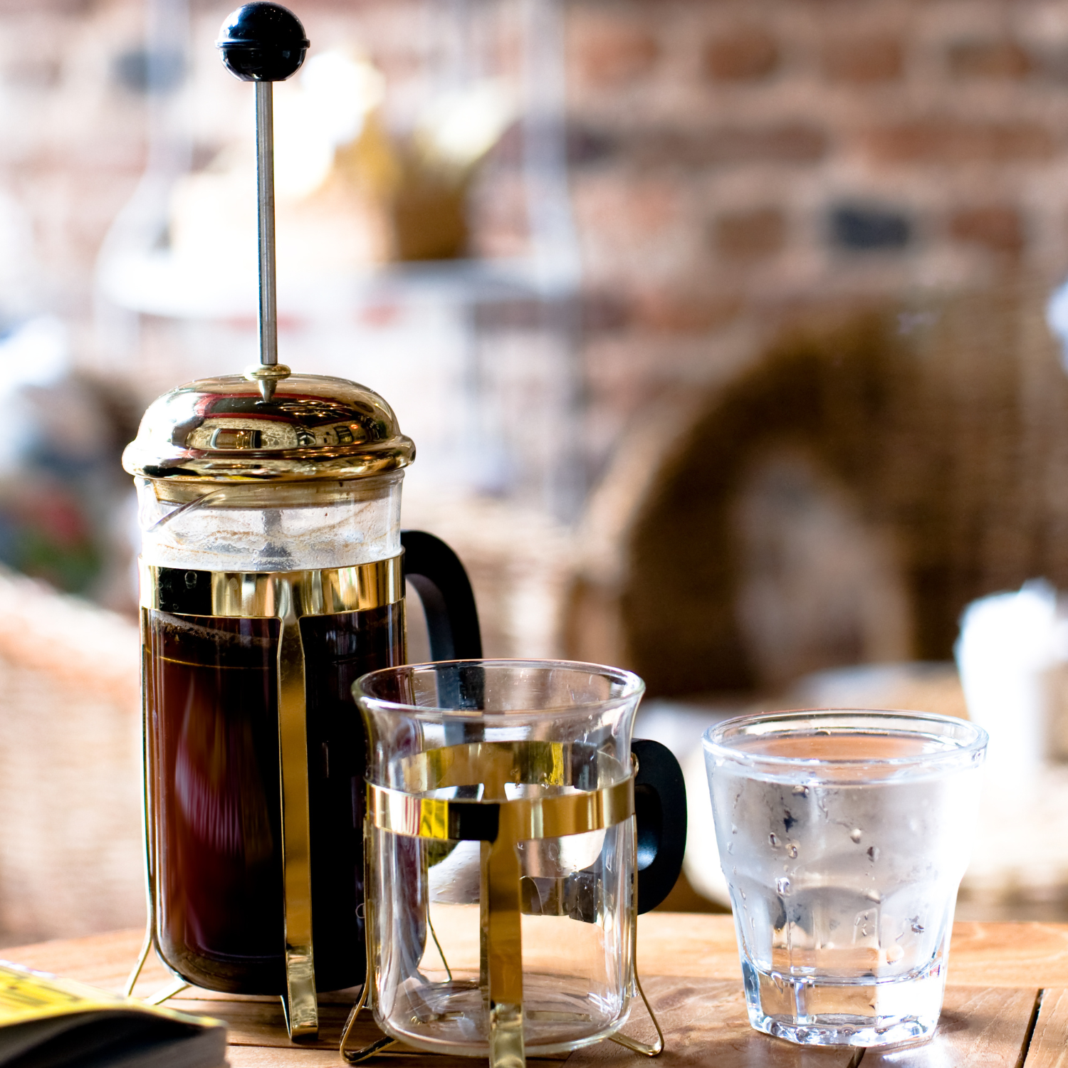 French Press brewing rich coffee from Huehuetenango, Guatemala on a wooden table, surrounded by a cup and a glass of water. A smooth and flavorful filter coffee made from single-origin beans. 