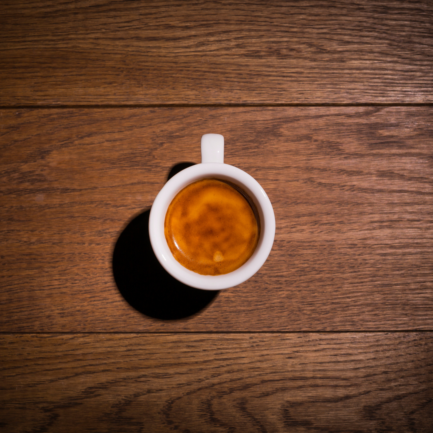 Top-down view of a perfect espresso in a white cup on a clean wooden table. Rich crema and deep aroma highlight this Colombian single-origin coffee, ideal for espresso lovers.