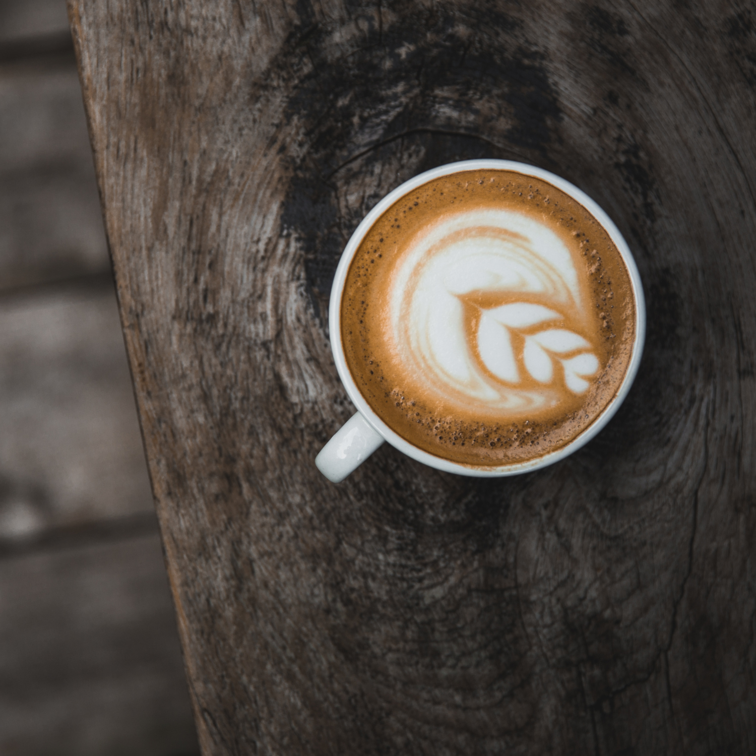 Top-down view of a flat white with intricate latte art in a white cup on a wooden table. Crafted from a Colombian single-origin coffee, perfect for espresso lovers.